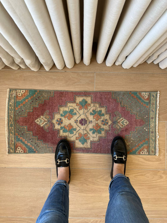 Add a pop of colour with vintage flair! Our vintage Turkish traditional distressed mini rug features greens, blues, purples, orange, taupes, and wine hues, with a tribal and Aztec central motif design. Hand-knotted and uniquely vintage, this antique rug adds timeless sophistication to your space, inspired by design styles reminiscent of Studio McGee and Amber Interiors. Perfect for bathmats, kitchen mats, or door entries