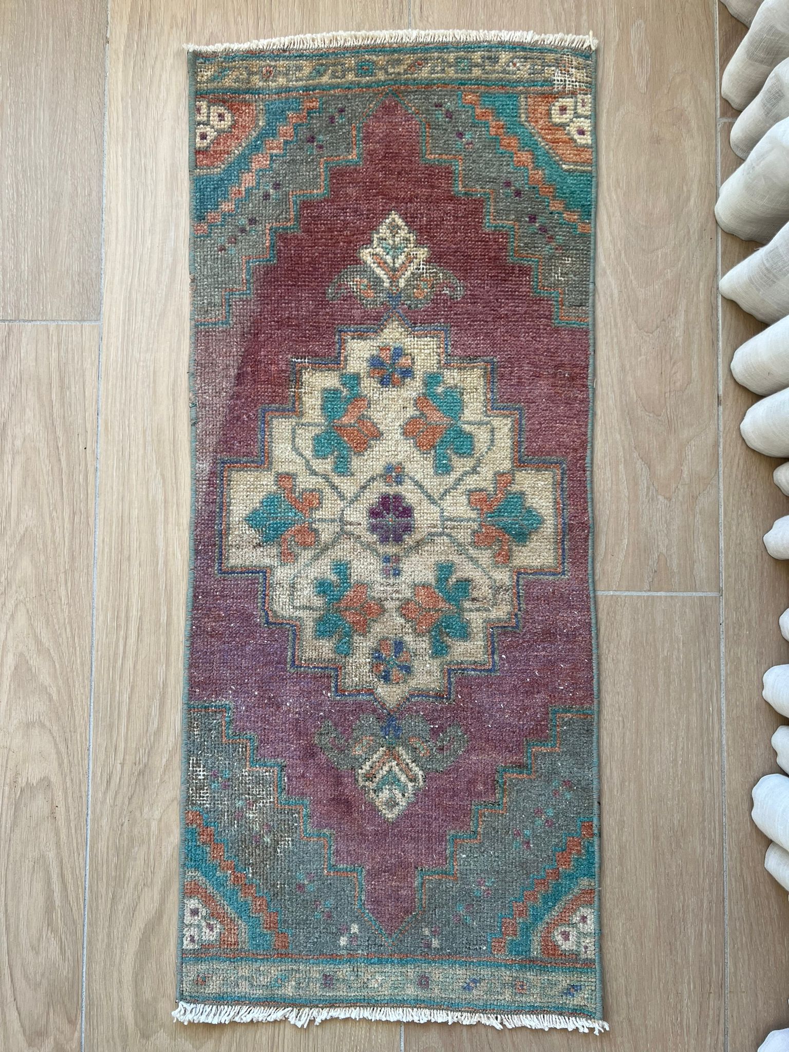 Add a pop of colour with vintage flair! Our vintage Turkish traditional distressed mini rug features greens, blues, purples, orange, taupes, and wine hues, with a tribal and Aztec central motif design. Hand-knotted and uniquely vintage, this antique rug adds timeless sophistication to your space, inspired by design styles reminiscent of Studio McGee and Amber Interiors. Perfect for bathmats, kitchen mats, or door entries
