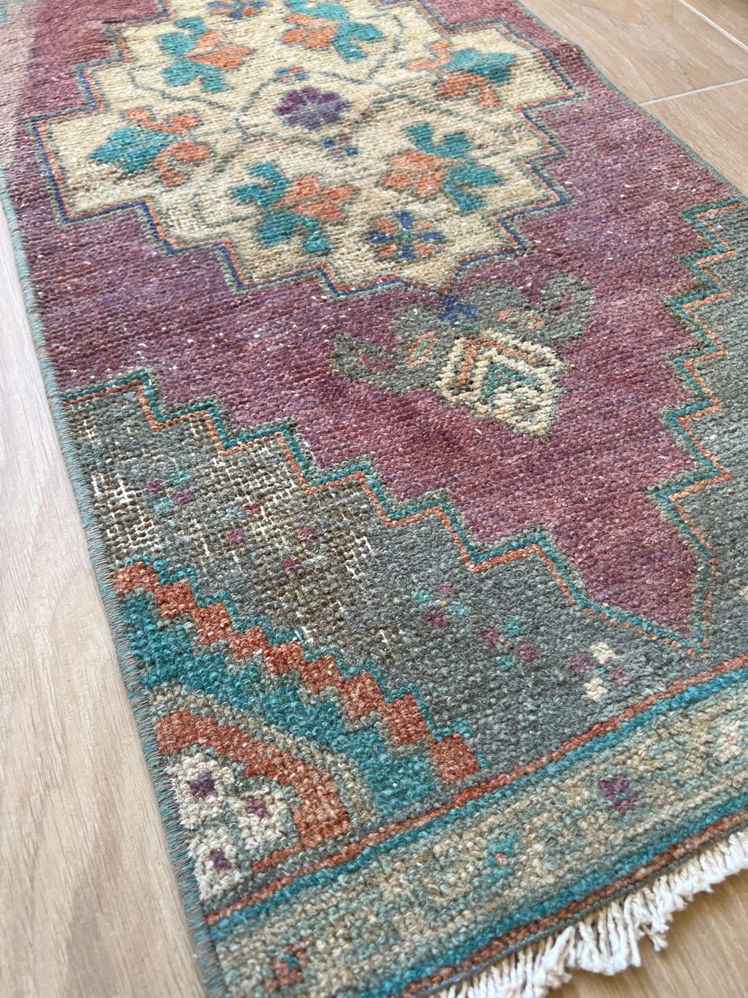 Add a pop of colour with vintage flair! Our vintage Turkish traditional distressed mini rug features greens, blues, purples, orange, taupes, and wine hues, with a tribal and Aztec central motif design. Hand-knotted and uniquely vintage, this antique rug adds timeless sophistication to your space, inspired by design styles reminiscent of Studio McGee and Amber Interiors. Perfect for bathmats, kitchen mats, or door entries