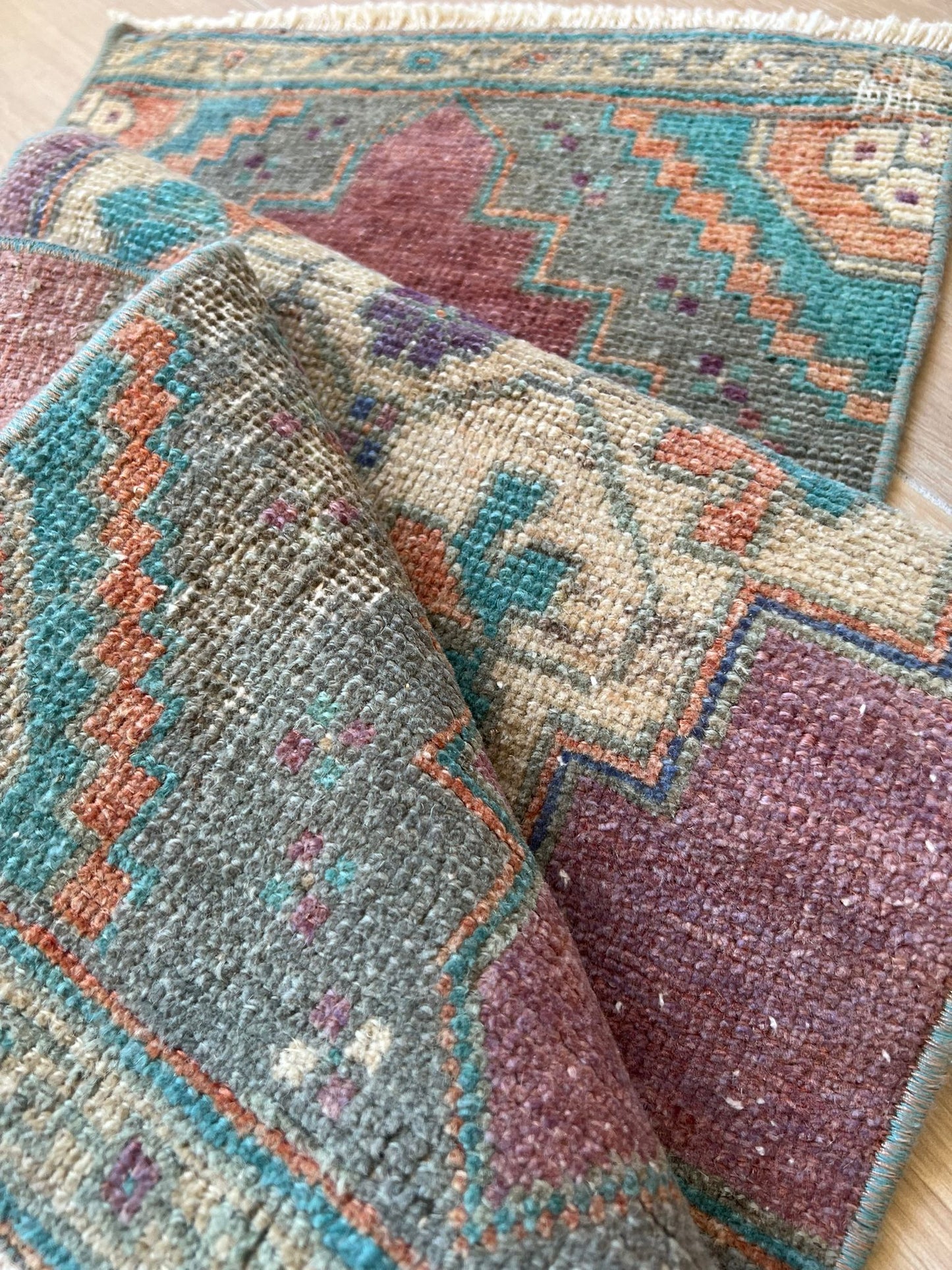 Add a pop of colour with vintage flair! Our vintage Turkish traditional distressed mini rug features greens, blues, purples, orange, taupes, and wine hues, with a tribal and Aztec central motif design. Hand-knotted and uniquely vintage, this antique rug adds timeless sophistication to your space, inspired by design styles reminiscent of Studio McGee and Amber Interiors. Perfect for bathmats, kitchen mats, or door entries