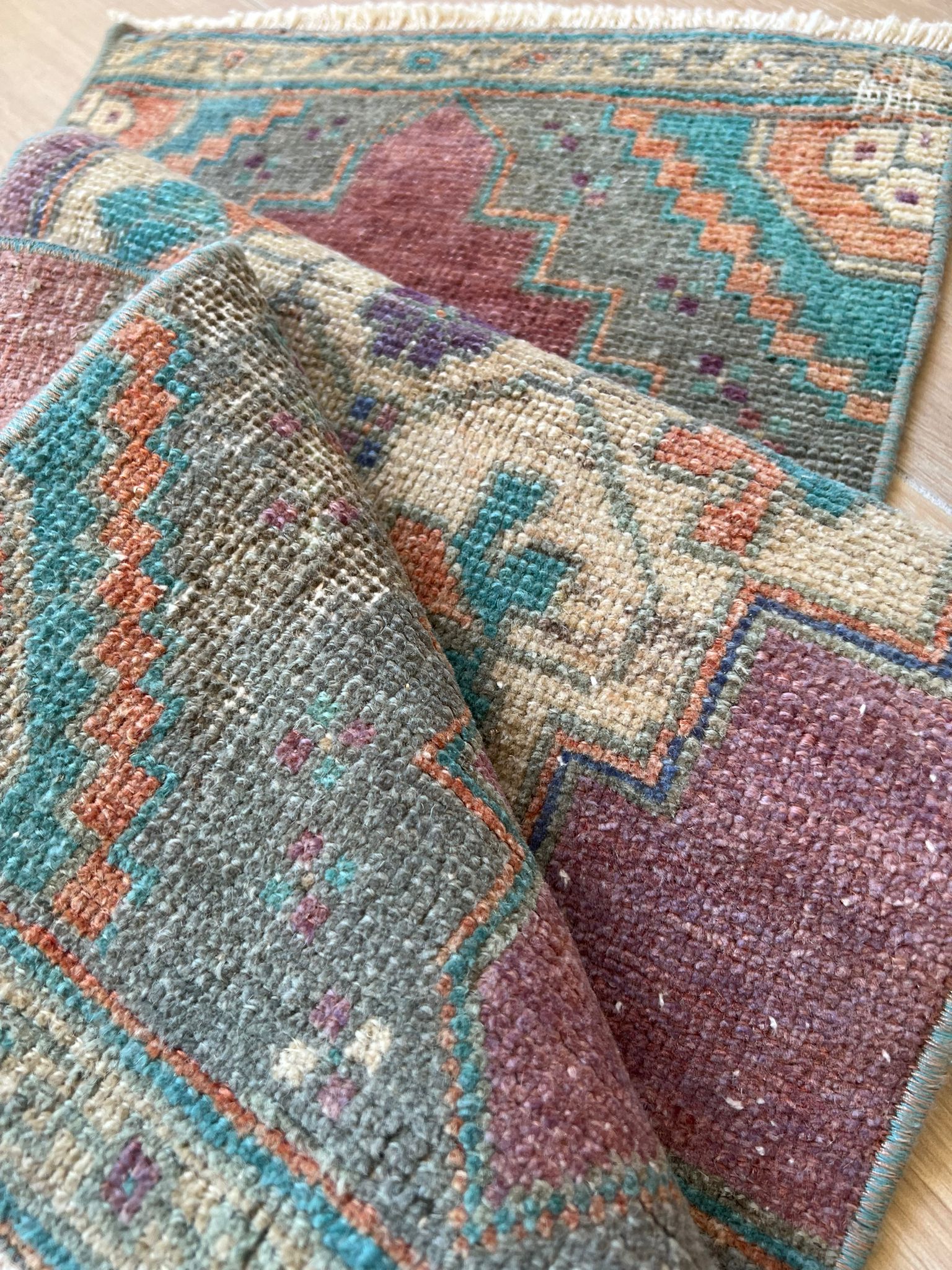 Add a pop of colour with vintage flair! Our vintage Turkish traditional distressed mini rug features greens, blues, purples, orange, taupes, and wine hues, with a tribal and Aztec central motif design. Hand-knotted and uniquely vintage, this antique rug adds timeless sophistication to your space, inspired by design styles reminiscent of Studio McGee and Amber Interiors. Perfect for bathmats, kitchen mats, or door entries